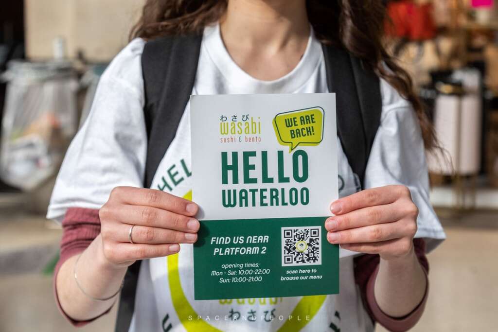 Person holding up a Wasabi food flyer in London Waterloo Station